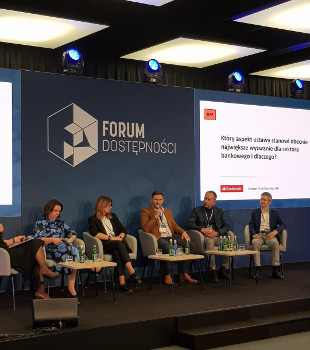 5 uczestników panelu siedzi na fotelach przy małych stolikach. 