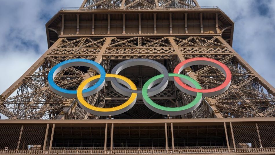 Dolny fragment Wieży Eiffla widziany z dołu, na jego tle 5 dużych kół olimpijskich